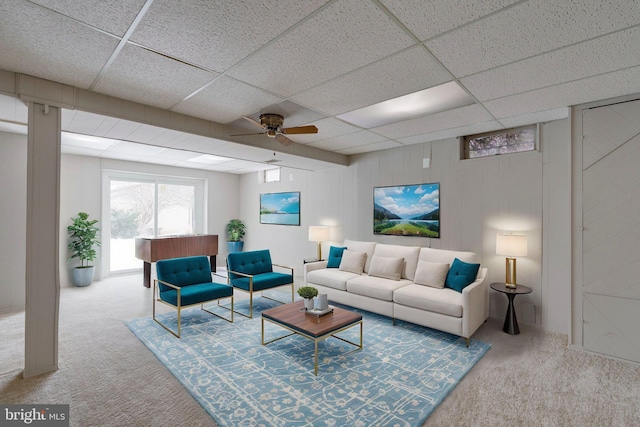 living room featuring light colored carpet, a drop ceiling, ceiling fan, and wood walls