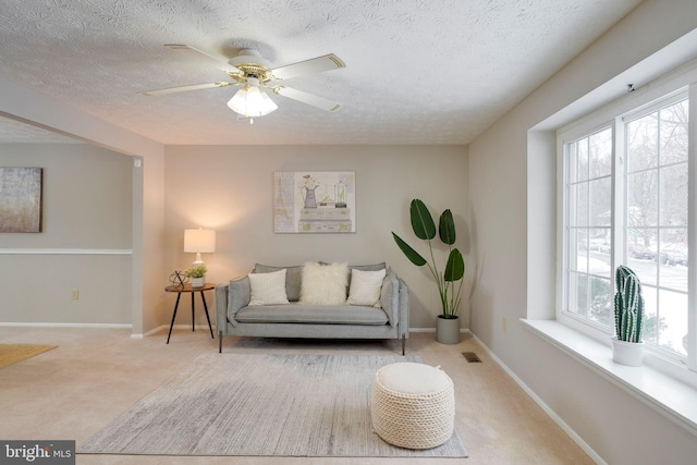 living area with a wealth of natural light, light colored carpet, and ceiling fan