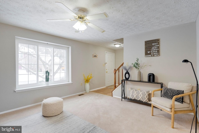 living area featuring ceiling fan, light carpet, and a textured ceiling