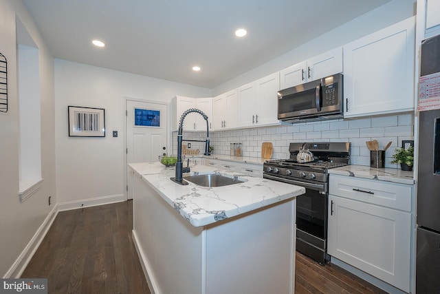 kitchen with white cabinetry, sink, light stone countertops, stainless steel appliances, and a kitchen island with sink