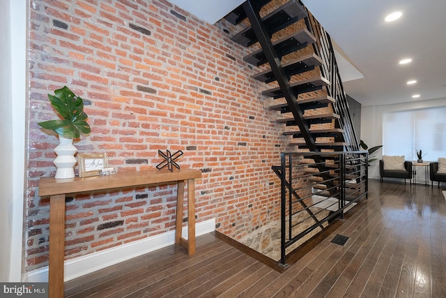 staircase with hardwood / wood-style floors and brick wall