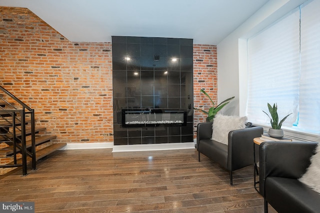 living room featuring a tile fireplace, wood-type flooring, and brick wall