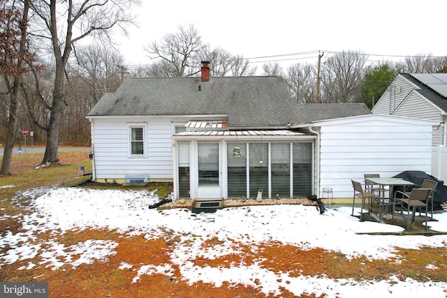 snow covered rear of property with a sunroom