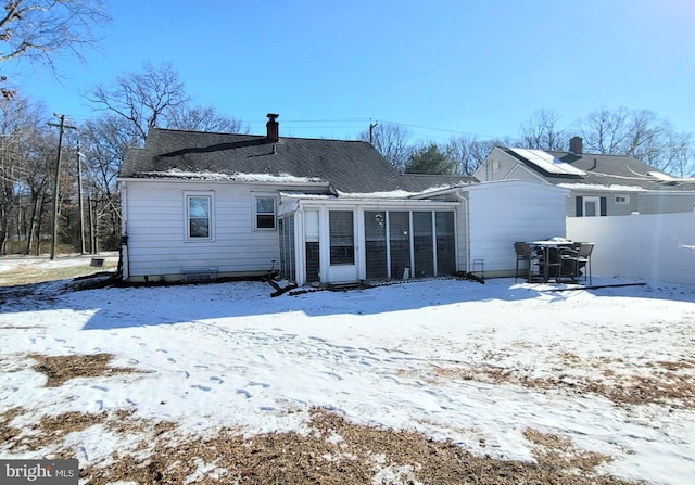 snow covered rear of property featuring a sunroom