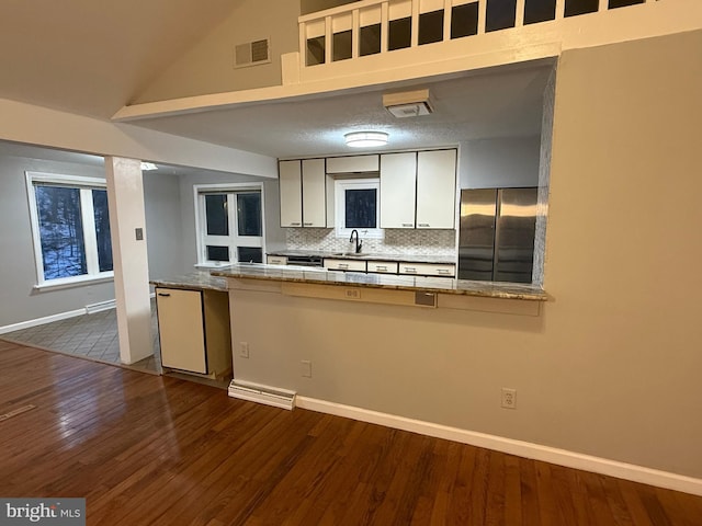 kitchen with decorative backsplash, stainless steel fridge, vaulted ceiling, dark wood-type flooring, and sink