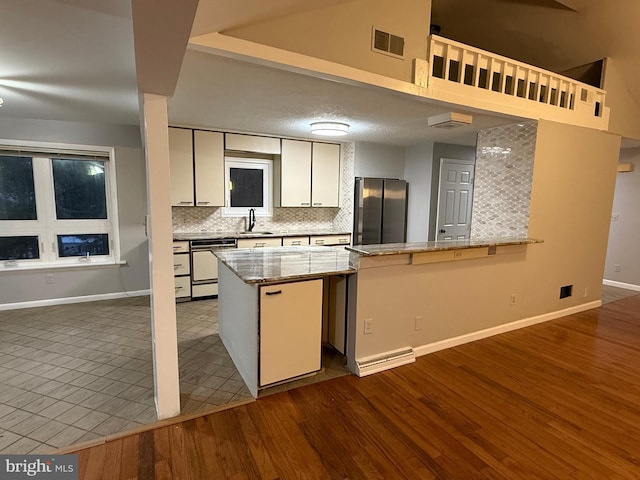 kitchen featuring kitchen peninsula, stainless steel fridge, white dishwasher, decorative backsplash, and white cabinets