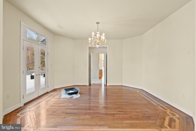 unfurnished dining area with a notable chandelier, light wood-type flooring, and french doors