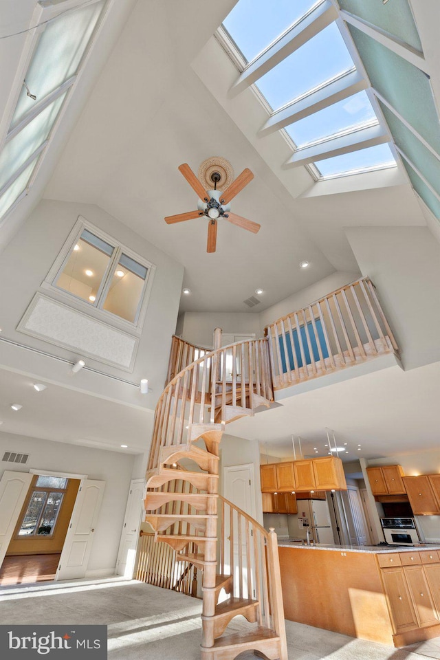 stairs featuring ceiling fan, high vaulted ceiling, and a skylight