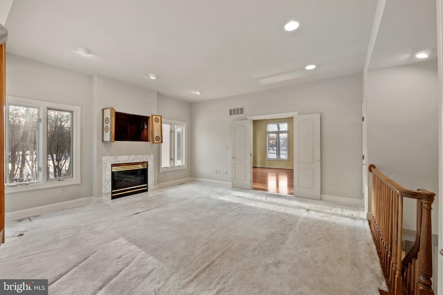 unfurnished living room featuring a healthy amount of sunlight, light colored carpet, and a high end fireplace