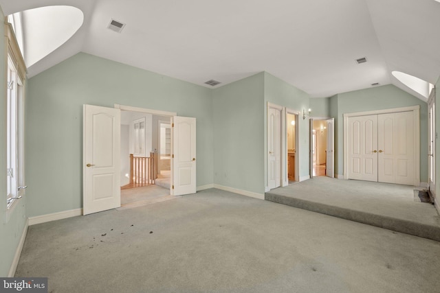 unfurnished bedroom featuring ensuite bathroom, light carpet, and vaulted ceiling