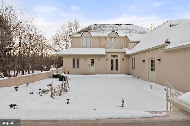 snow covered house featuring a balcony and french doors