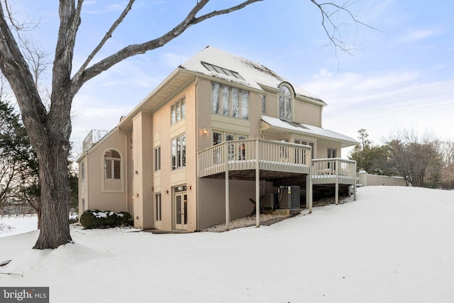 snow covered property with central air condition unit and a deck