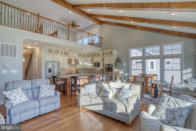 living room with ceiling fan, high vaulted ceiling, beamed ceiling, and light hardwood / wood-style floors