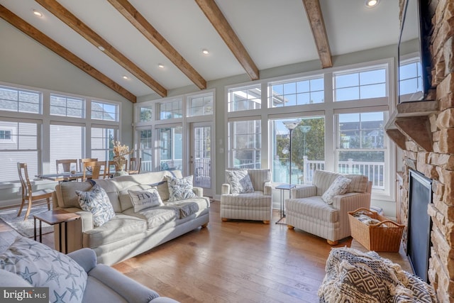 sunroom / solarium featuring vaulted ceiling with beams and a stone fireplace