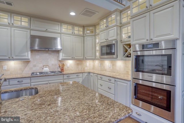 kitchen featuring appliances with stainless steel finishes, sink, white cabinetry, and wall chimney range hood