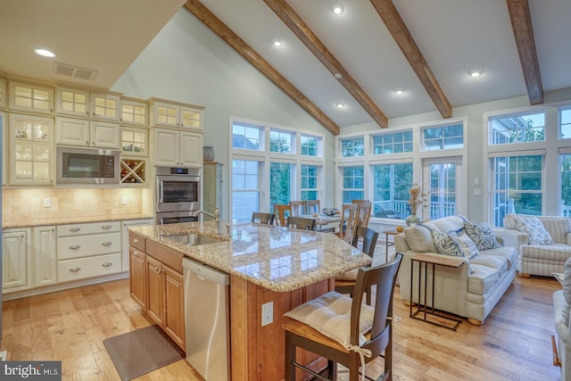 kitchen with stainless steel appliances, decorative backsplash, high vaulted ceiling, light stone counters, and a center island with sink