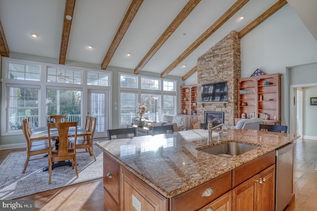 kitchen featuring a fireplace, sink, high vaulted ceiling, stainless steel dishwasher, and a center island with sink