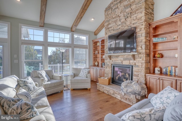 living room with high vaulted ceiling, hardwood / wood-style floors, beamed ceiling, and a stone fireplace