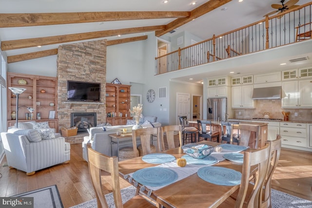 dining space featuring light hardwood / wood-style floors, ceiling fan, a fireplace, high vaulted ceiling, and beamed ceiling