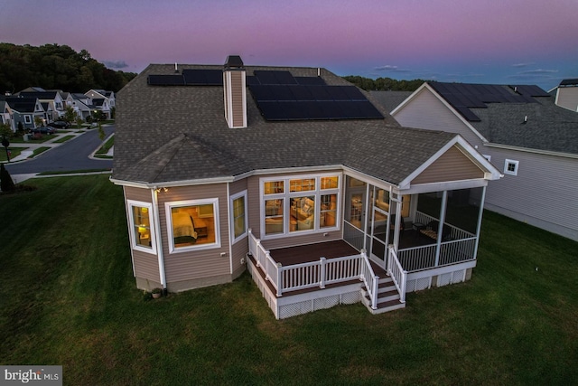 back house at dusk with solar panels and a sunroom