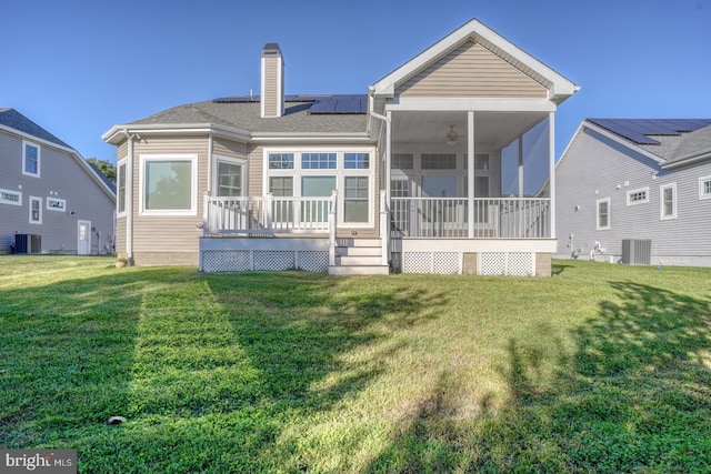 rear view of property featuring central AC unit, a lawn, a sunroom, and solar panels