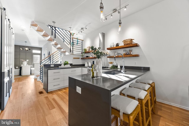 kitchen featuring sink, light hardwood / wood-style flooring, white cabinetry, and hanging light fixtures