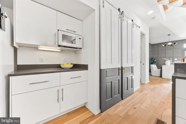 kitchen featuring light hardwood / wood-style floors, white cabinetry, decorative light fixtures, and a barn door