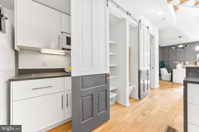 interior space with a notable chandelier, a barn door, light hardwood / wood-style flooring, and white cabinetry