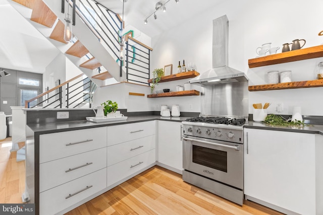 kitchen with kitchen peninsula, wall chimney exhaust hood, high end range, light hardwood / wood-style floors, and white cabinets