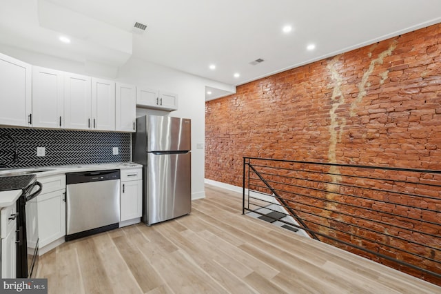 kitchen featuring backsplash, light hardwood / wood-style floors, white cabinetry, stainless steel appliances, and brick wall