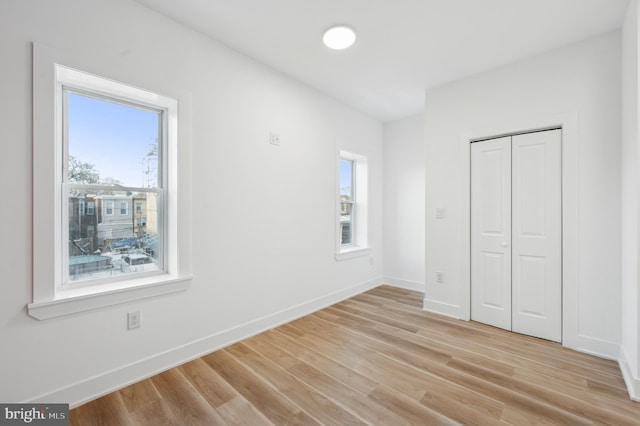 unfurnished bedroom featuring multiple windows, light wood-type flooring, and a closet