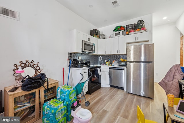 kitchen with appliances with stainless steel finishes, tasteful backsplash, white cabinetry, and light hardwood / wood-style floors