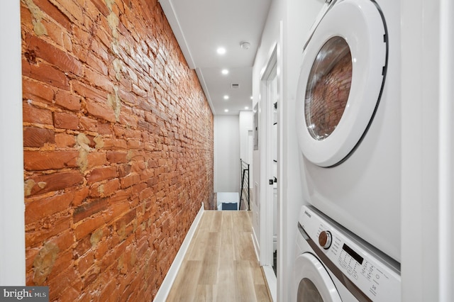 laundry room with stacked washer / drying machine, light wood-type flooring, and brick wall