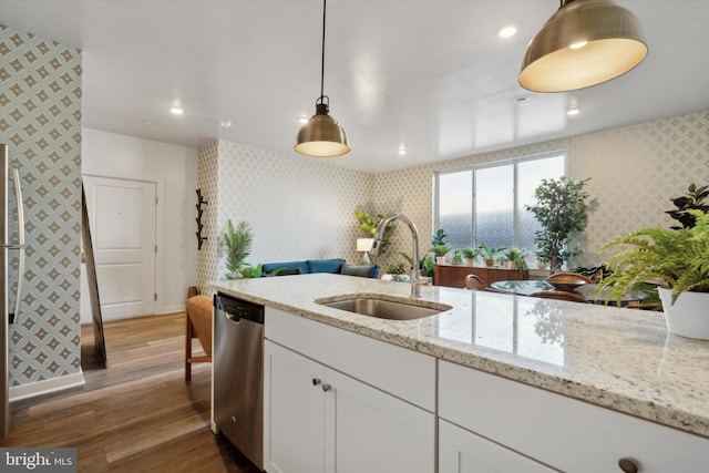 kitchen with light stone counters, stainless steel dishwasher, sink, white cabinets, and hanging light fixtures