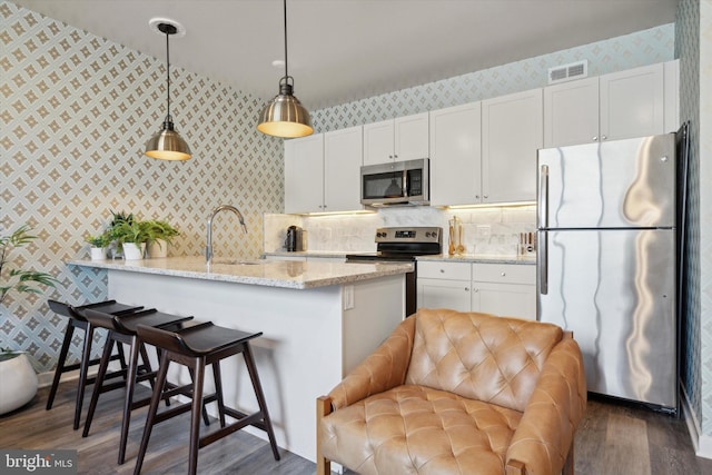 kitchen with light stone countertops, stainless steel appliances, sink, pendant lighting, and white cabinets