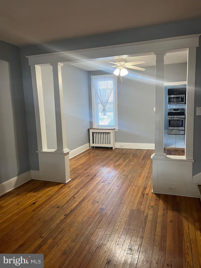 spare room featuring radiator heating unit, hardwood / wood-style flooring, ornate columns, and ceiling fan