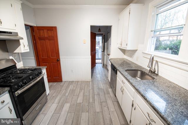 kitchen with appliances with stainless steel finishes, ornamental molding, white cabinets, light hardwood / wood-style flooring, and sink