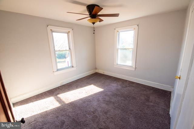 spare room with ceiling fan and dark colored carpet