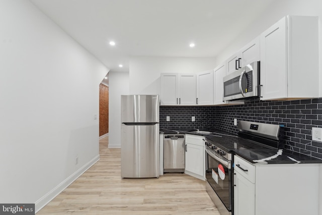 kitchen featuring white cabinets, decorative backsplash, appliances with stainless steel finishes, and dark stone counters