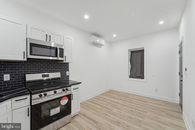 kitchen featuring decorative backsplash, light wood-type flooring, stainless steel appliances, a wall mounted AC, and white cabinetry