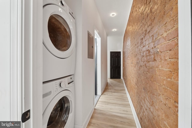 clothes washing area featuring stacked washer and dryer, brick wall, and light wood-type flooring