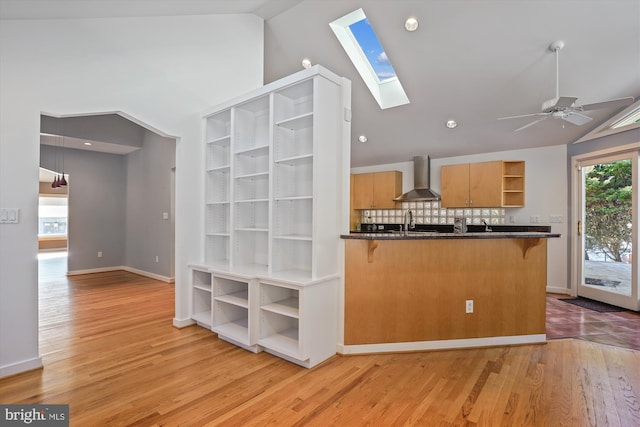 kitchen featuring kitchen peninsula, wall chimney range hood, a breakfast bar, backsplash, and ceiling fan