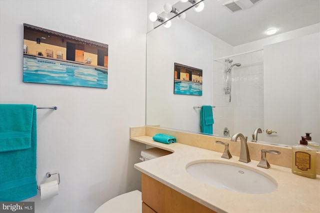 bathroom with toilet, a tile shower, and vanity