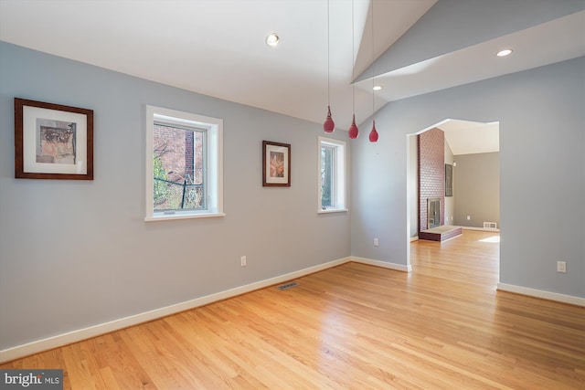 spare room featuring a fireplace, light wood-type flooring, and vaulted ceiling