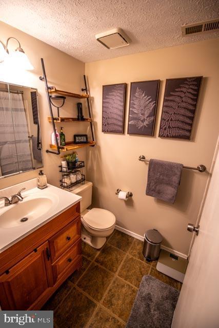 bathroom with toilet, vanity, a textured ceiling, and walk in shower