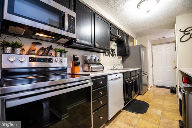 kitchen featuring stainless steel appliances, a textured ceiling, sink, and light tile patterned floors