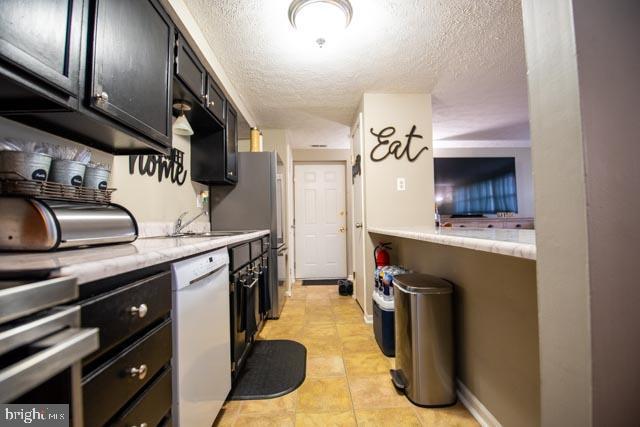 kitchen with a textured ceiling, dishwasher, light stone countertops, and stainless steel refrigerator