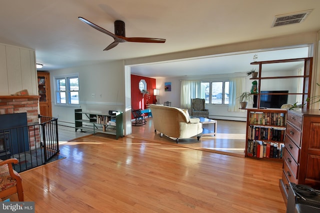 living room with ceiling fan, a brick fireplace, and light wood-type flooring