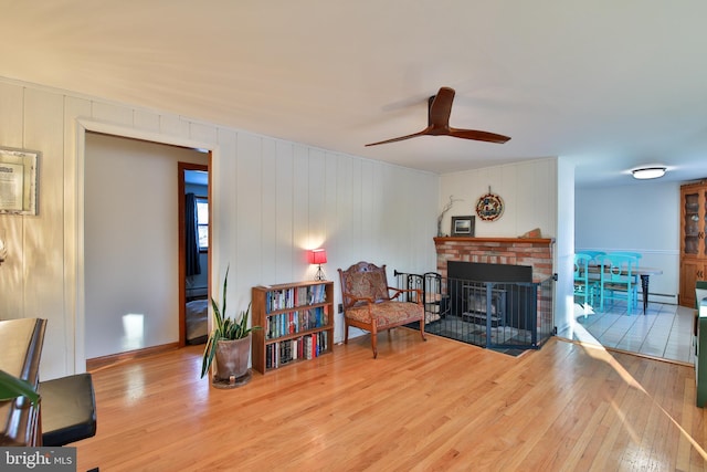 living area with wood-type flooring, ceiling fan, and a fireplace