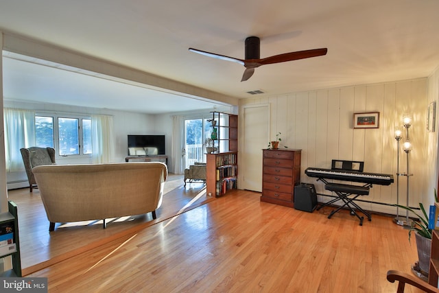 living room with a baseboard heating unit, light hardwood / wood-style floors, ceiling fan, and wood walls